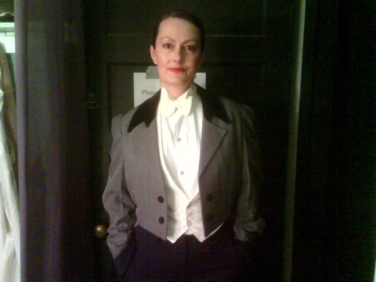 A woman in a tuxedo standing in front of a door.