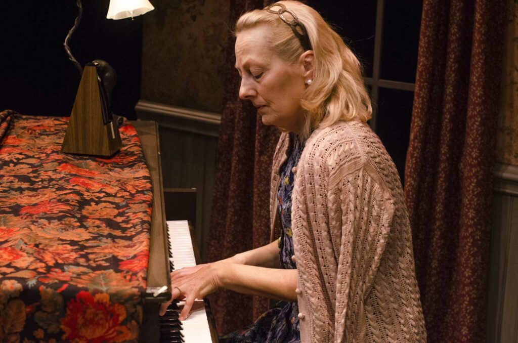 A woman playing a piano in front of a lamp.